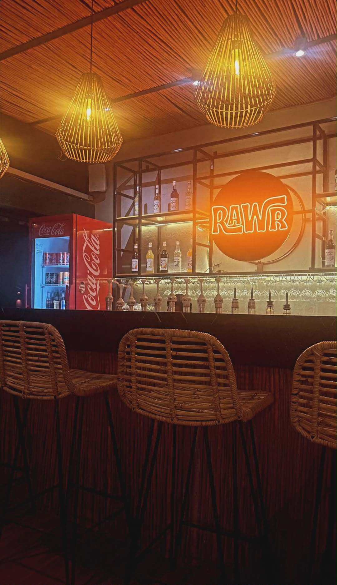 Rawr Cafe bar area with rattan chairs and RAWR neon sign